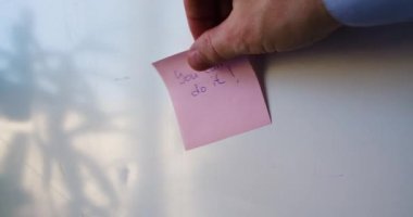 Yapabilirsin. Bir erkeğin eli bir hatırlatma çıkartması yapıştırıyor..