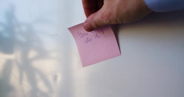 You can do it - a mans hand is pasting a reminder sticker. — Stockvideo
