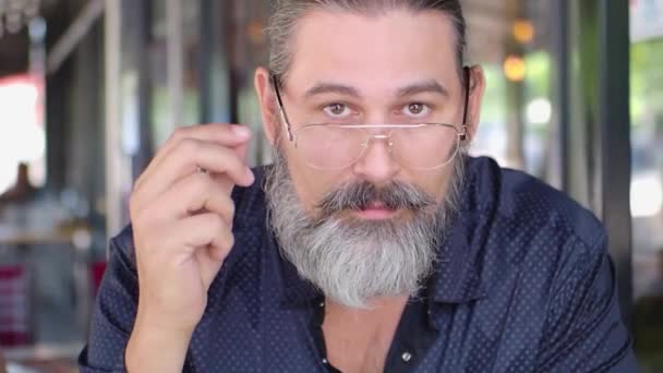 Bearded middle-aged man takes off his glasses, looks at the camera and smiles. Slow motion. — Stockvideo