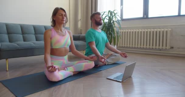 Couple meditating at home inin front of laptop with online yoga tutorial. 4K footage. — Stockvideo