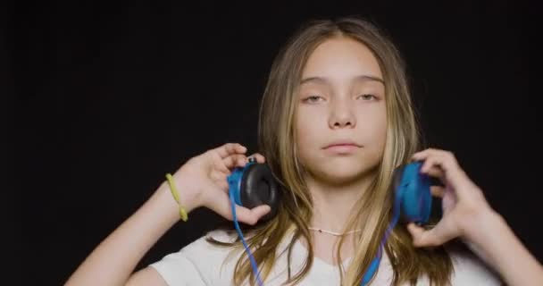 Teenage girl wearing headphones and listening to the hard rock music over black background. — Stockvideo