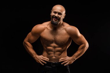 Brutal bald man with a beard stands and smiles - photo on a black background.