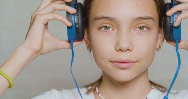 Adolescente chica pone en los auriculares, mirando a la cámara y sonriendo. — Vídeo de stock