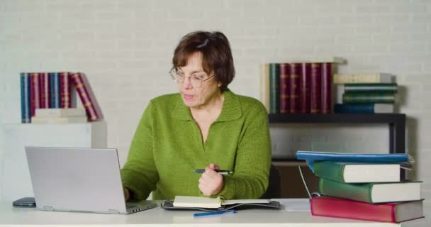 Senor adult woman in a green sweater works in front of a laptop monitor in the evening office. — Stockvideo