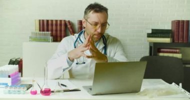 Orta yaşlı bir doktor klinikte otururken araştırma raporuyla düşünür..