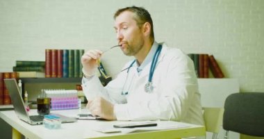 Orta yaşlı bir doktor klinikte otururken araştırma raporuyla düşünür..