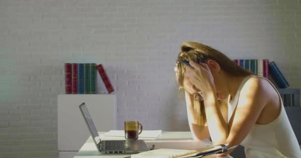 Eine junge Frau im Büro - nimmt ihre Brille, ihr Headset ab und fasst sich an den Kopf. Sie hat starke Kopfschmerzen und ist sehr müde. — Stockvideo