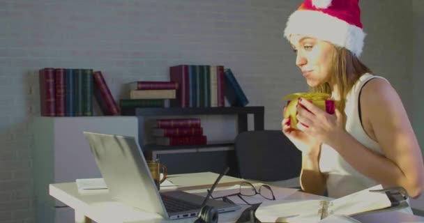Junge Frau an Heiligabend in Weihnachtsmütze im Amt - sie erhielt ein Geschenk und bedankt sich bei ihrem Mann während eines Online-Videoanrufs. — Stockvideo