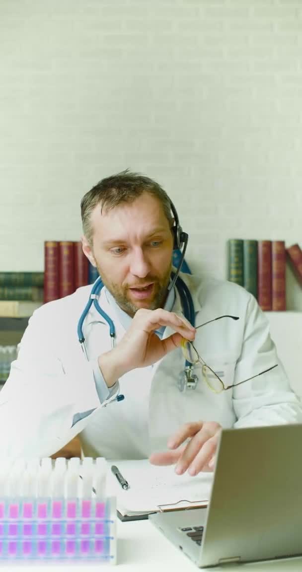 Vídeo vertical de um médico fala sobre a última pesquisa durante uma videochamada online. Ele tirou os óculos e gesticulou ativamente, falando sobre as descobertas.. — Vídeo de Stock