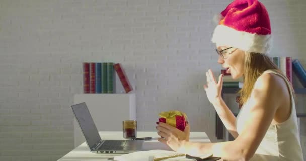 Noel arifesinde Santa Hat 'taki kadın bir hediye aldı ve online video görüşmesi sırasında erkek arkadaşına teşekkür etti.. — Stok video