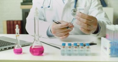 Doktorun elinde bir aşı örneğiyle test tüpünün içinde laboratuarda bir rapor hazırlıyor. Modern aşıların geliştirilmesi üzerine araştırma.