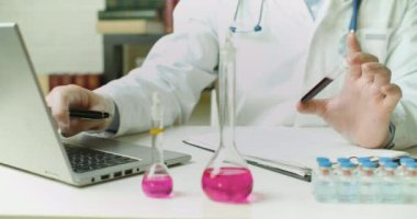 Test tüpündeki kan örneğiyle bir doktorun ellerine yakın çekim. Laboratuvarda bir rapor yazıyor..