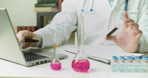 Κοντινό πλάνο ενός γιατρού χέρια με ένα δείγμα αίματος σε δοκιμαστικό σωλήνα - γράφει μια έκθεση στο εργαστήριο. — Αρχείο Βίντεο