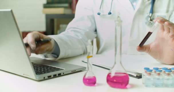 एक परीक्षण ट्यूब में रक्त नमूना के साथ डॉक्टर हाथों का डॉली शॉट वह प्रयोगशाला में एक रिपोर्ट लिखता है . — स्टॉक वीडियो