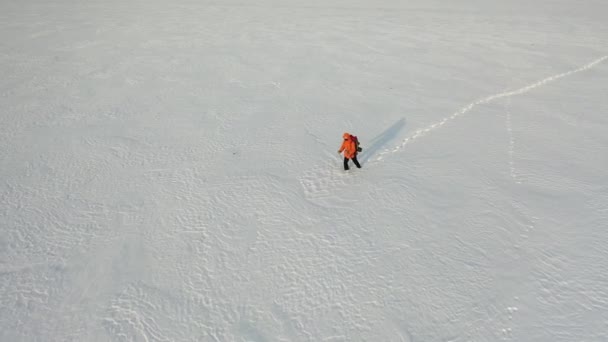 Вид с дрона - одиночка с рюкзаком шагает по заснеженной пустыне. — стоковое видео
