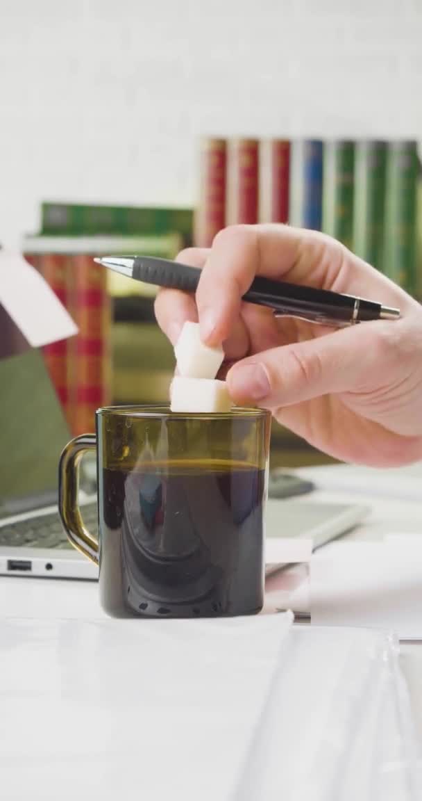 A man adds sugar to coffee at the workplace in the office and stirs it by pen. — Stock Video
