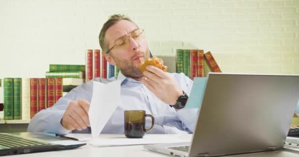 Мужчина средних лет сидит в офисе - ест нездоровую пищу, делает бумажный самолет и летает на нем. — стоковое видео