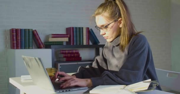 Gözlüklü beyaz bir kadın laptop monitörünün önünde çalışıyor. Raporu kontrol eder ve taslaklarda değişiklikler yapar.. — Stok video
