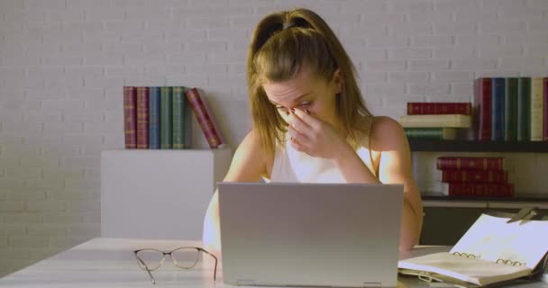 Una joven cansada se sienta frente a un monitor portátil, se quita las gafas y masajea el puente de la nariz. Concepto de fecha límite. — Vídeo de stock