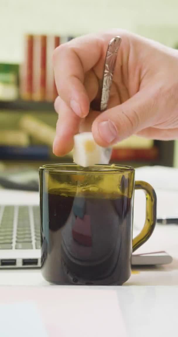 Ένα αρσενικό χέρι προσθέτει ζάχαρη στον καφέ στο χώρο εργασίας στο γραφείο και το ανακατεύει.. — Αρχείο Βίντεο