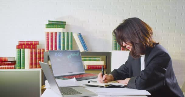 Analista de negocios está trabajando con el ordenador portátil - ella toma notas mientras revisa los formularios de impuestos y los informes de existencias. — Vídeo de stock