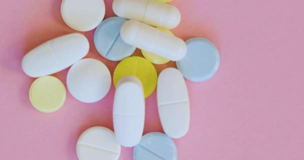 Detailní záběr, rotace - modré, bílé a žluté pilulky na růžovém pozadí. — Stock video