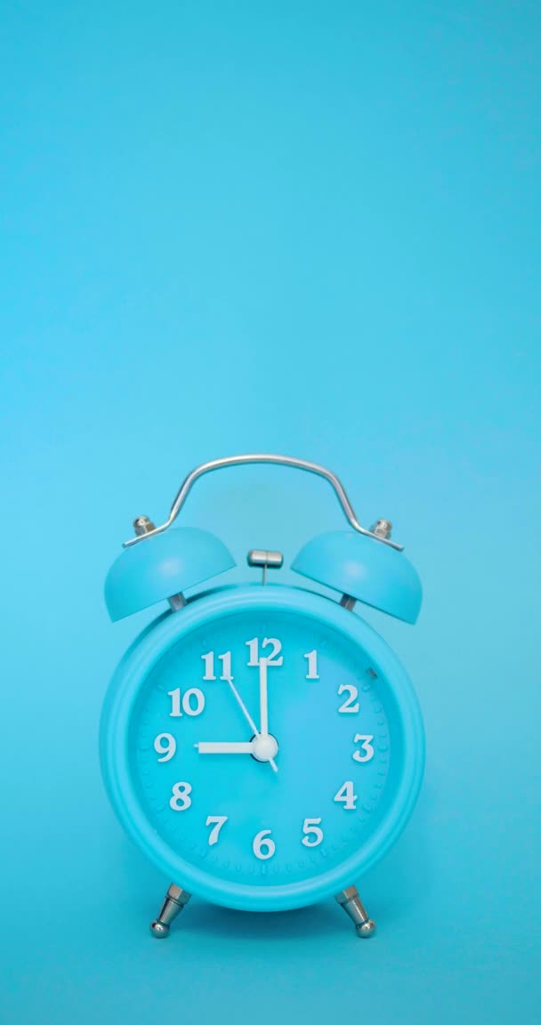 Blue alarm clock on a blue background rings at 9 AM - vertical video. — Stock Video
