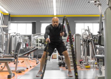 Orta yaşlı bir adamın spor salonunda iplerle sıkı antrenman yaptığı fotoğraf..