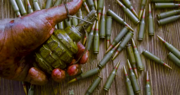 Guerra, muerte y suicidio: la mano ensangrentada de un soldado o rebelde con una granada sobre el fondo de una mesa de madera cubierta de munición. — Vídeos de Stock