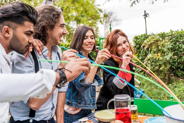 group of multi-cultural friends having fun at the garden party sucking beer from colorful straws from a cooler
