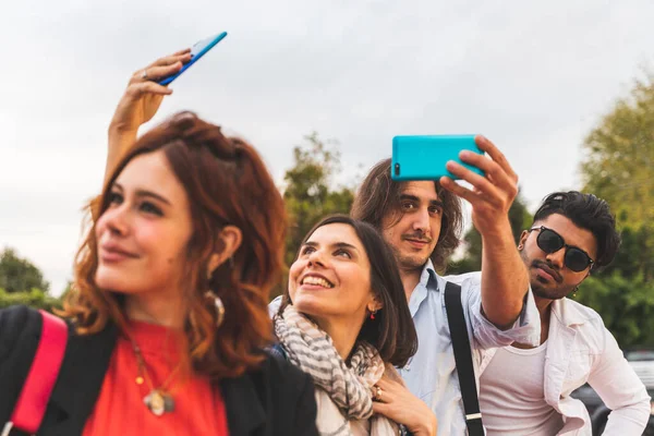 group of multi-cultural best friends take a selfie with smart phones outdoors - Focus on man with blue phone