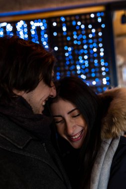 Akşamları aydınlık dükkanın önünde yürüyen genç çift sıcak kıyafetler ve eşarplar takıyor.