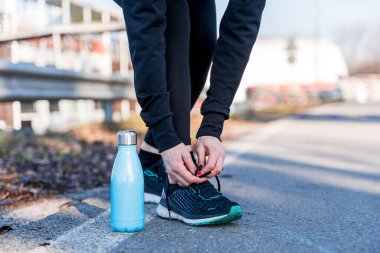 Genç bayan koşucu ayakkabılarını asfalt yolda bağlıyor. Sağlık ve sağlık kavramı.