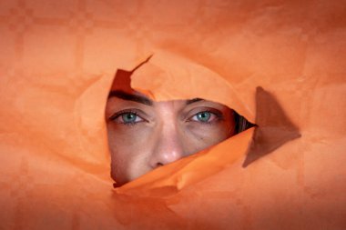 Çekici genç bir kadının portresi portakal rengi bir kağıdın içindeki delikten çıkıyor.