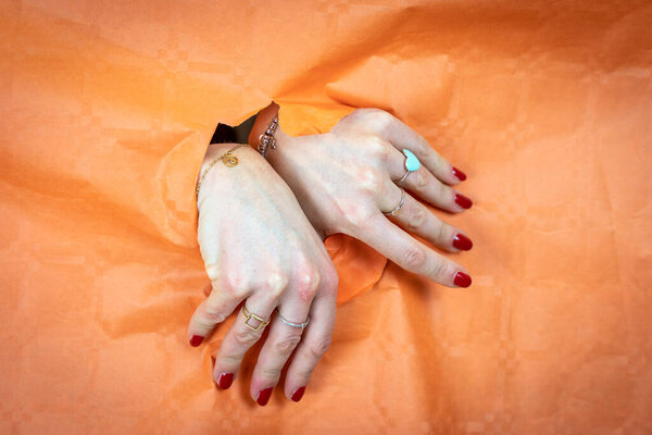 human hands of woman is coming out of a hole in a sheet of orange paper