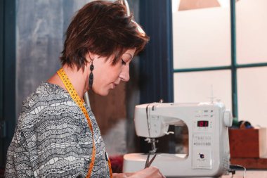 Genç terzi atölyedeki dikiş makinesiyle çalışıyor.