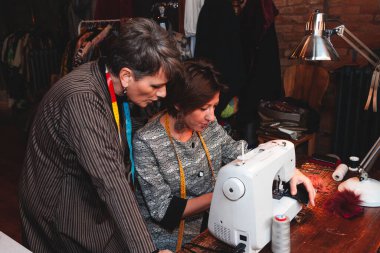 İki terzi atölyedeki dikiş makinesiyle çalışıyor.