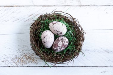 Beyaz ahşap arka planda bir yuvanın içinde üç dekoratif paskalya yumurtası.