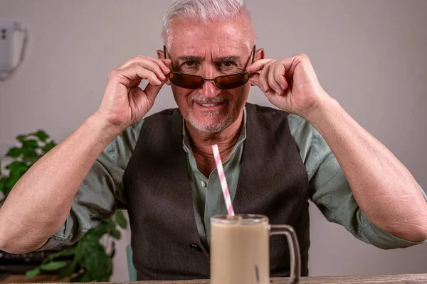 Dorywczo Ubrany Dojrzały Mężczyzna Okularach Przeciwsłonecznych Siedzi Przy Stole Pije — Zdjęcie stockowe