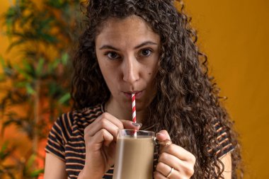 pretty woman with curly hair sitting on a table drinking cold coffee through a straw