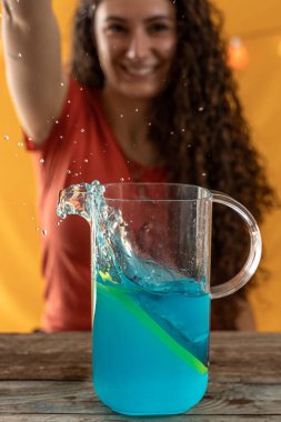 Genç bir kadın mavi kokteyl dolu bir sürahiye akıllı telefon atıyor. Stüdyo fotoğrafı.