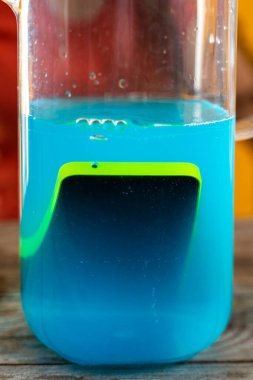 Genç bir kadın mavi kokteyl dolu bir sürahiye akıllı telefon atıyor. Stüdyo fotoğrafı.