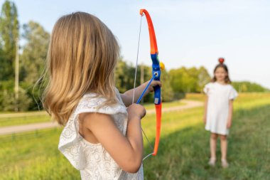 Sevimli küçük kız parkta kız kardeşiyle oyuncak bir yay ve okla oynuyor.