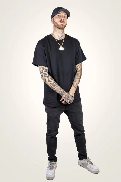 tattooed rap singer posing in studio wearing black clothes on a white background