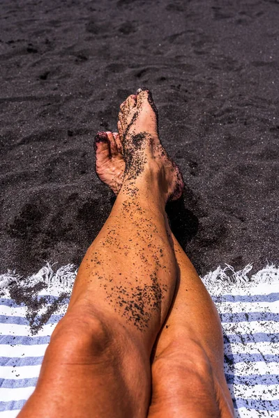 closeup of feet of man feet lying on a volcanic black tropical beach - summer vacation concept