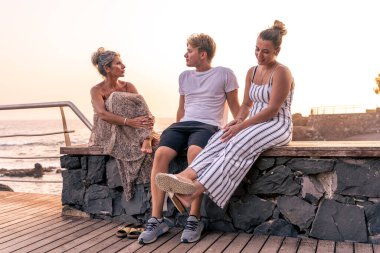 beautiful mother with her two twenty year old sons take a break by the sea at sunset - summer vacation concept