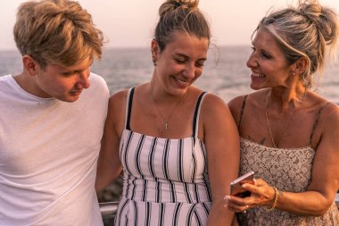 beautiful mother with her two twenty year old sons take a break by the sea at sunset - summer vacation concept