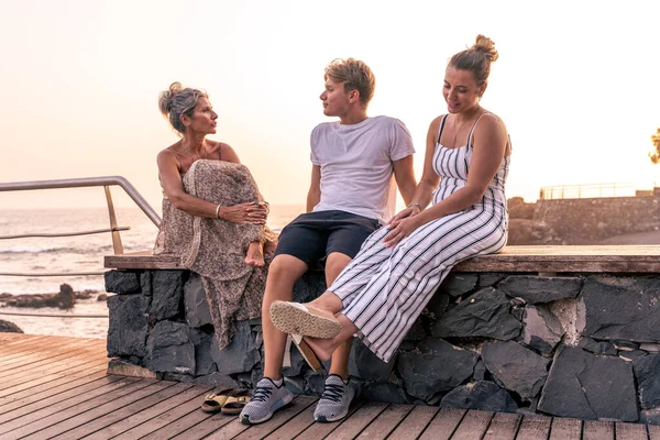 beautiful mother with her two twenty year old sons take a break by the sea at sunset - summer vacation concept