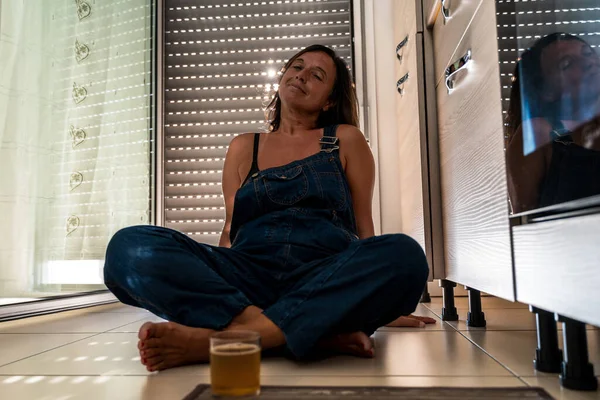 image of a beautiful middle aged woman drinking a cocktail sitting in her apartment - Mature woman dressed a dungarees in his home - Concept about body positivity self esteem and body acceptance