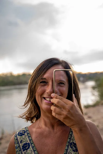 picture of beautiful middle aged lady using smartphone on the banks of the river at sunset